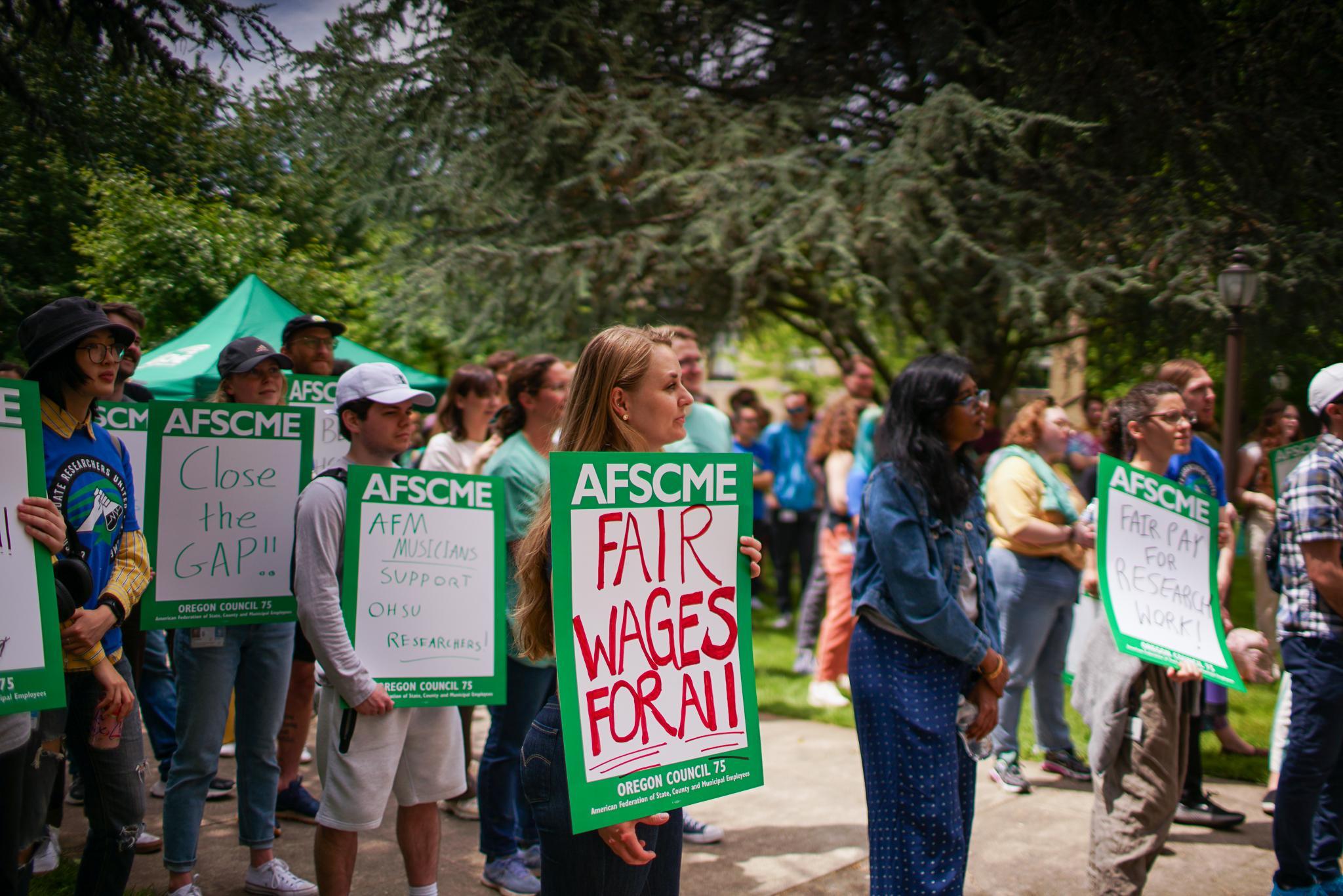 Group of research workers dressed in green, holding signs at a rally in front of OHSU